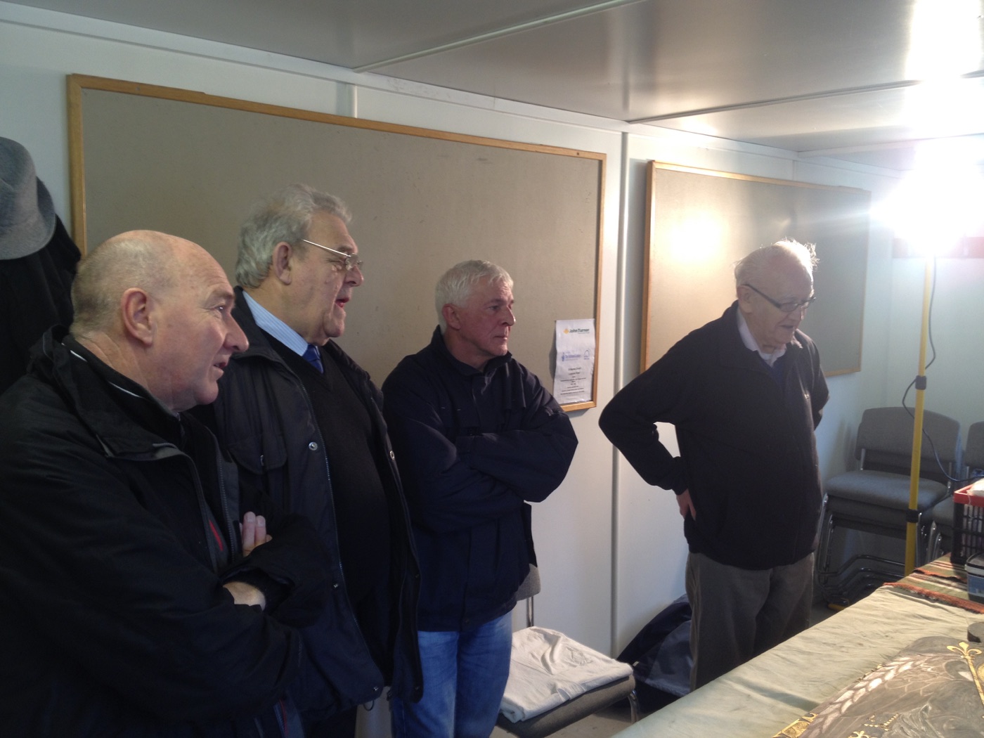 Four workshop visitors examining a reredos panel under a work lamp in the site office