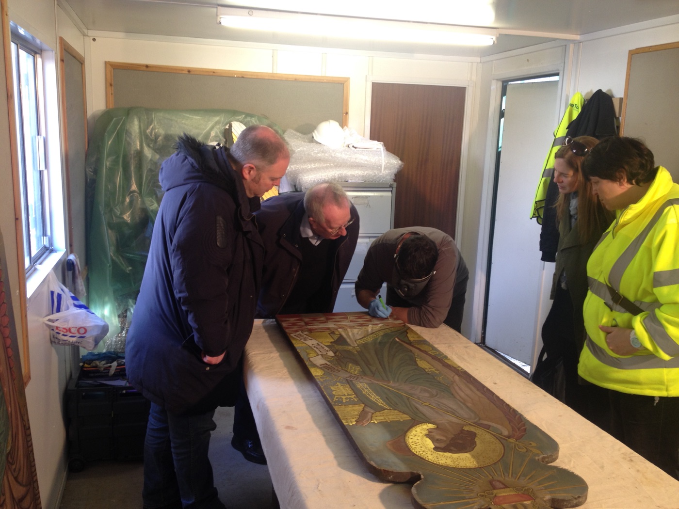 Silvano Cioci-Faux cleaning the altar panel with a head-mounted magnifier while the workshop group watches