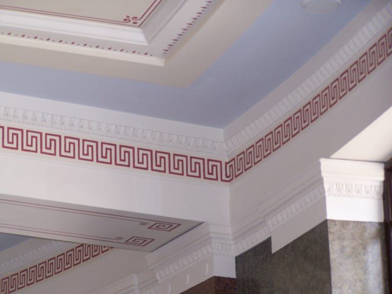 Historic Greek key stencil on a cornice band beside ornate ceiling mouldings